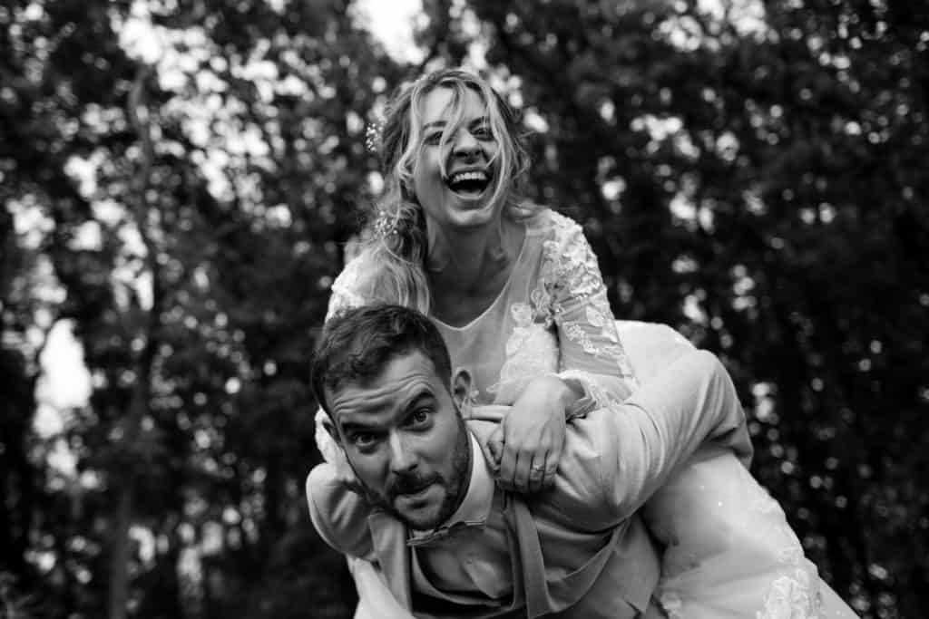 La mariée souriante est sur le dos du marié. Photo en noir et blanc.